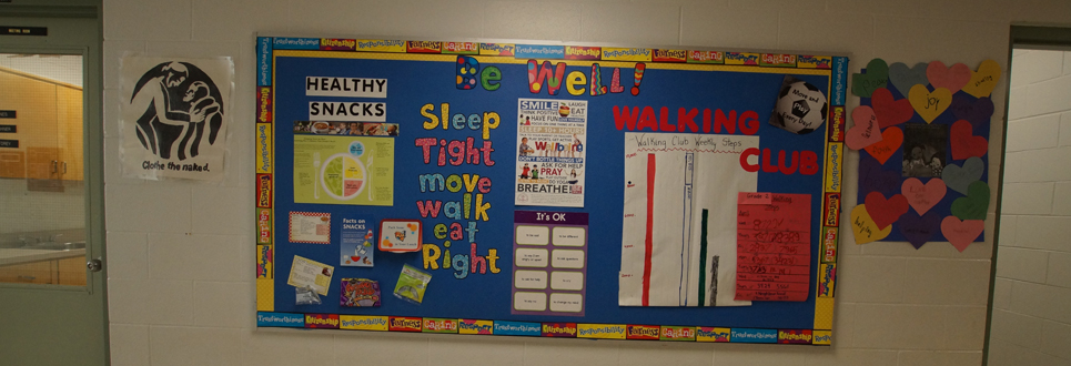 Bulletin board with the header, "Be Well" and is filled with various ways to stay healthy such as, "Healthy Snacks", "Walking Club" and "Sleep tight, move, walk, eat right" posted.