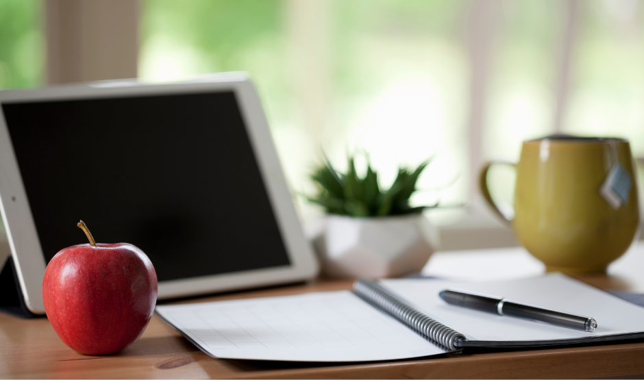 Open laptop on a desk with an apple beside it